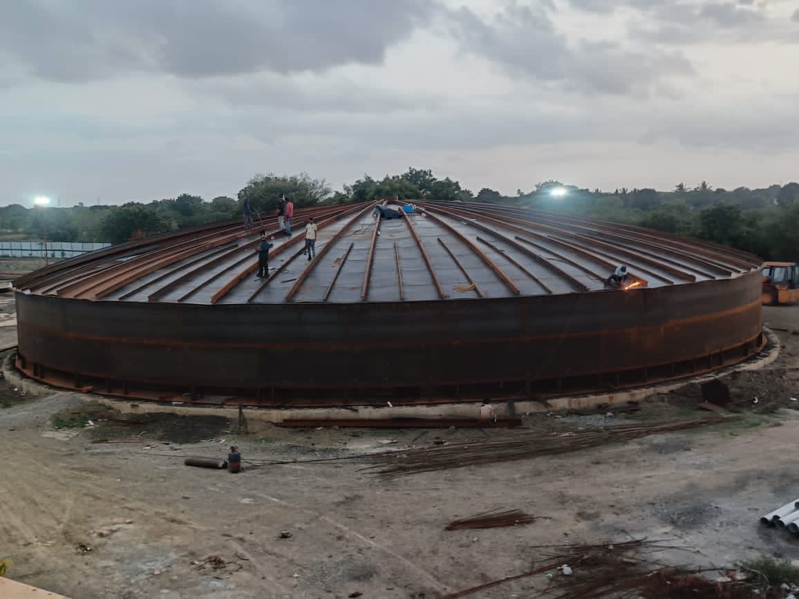 Main digester under construction: workers erecting the steel roof of the tank at dusk